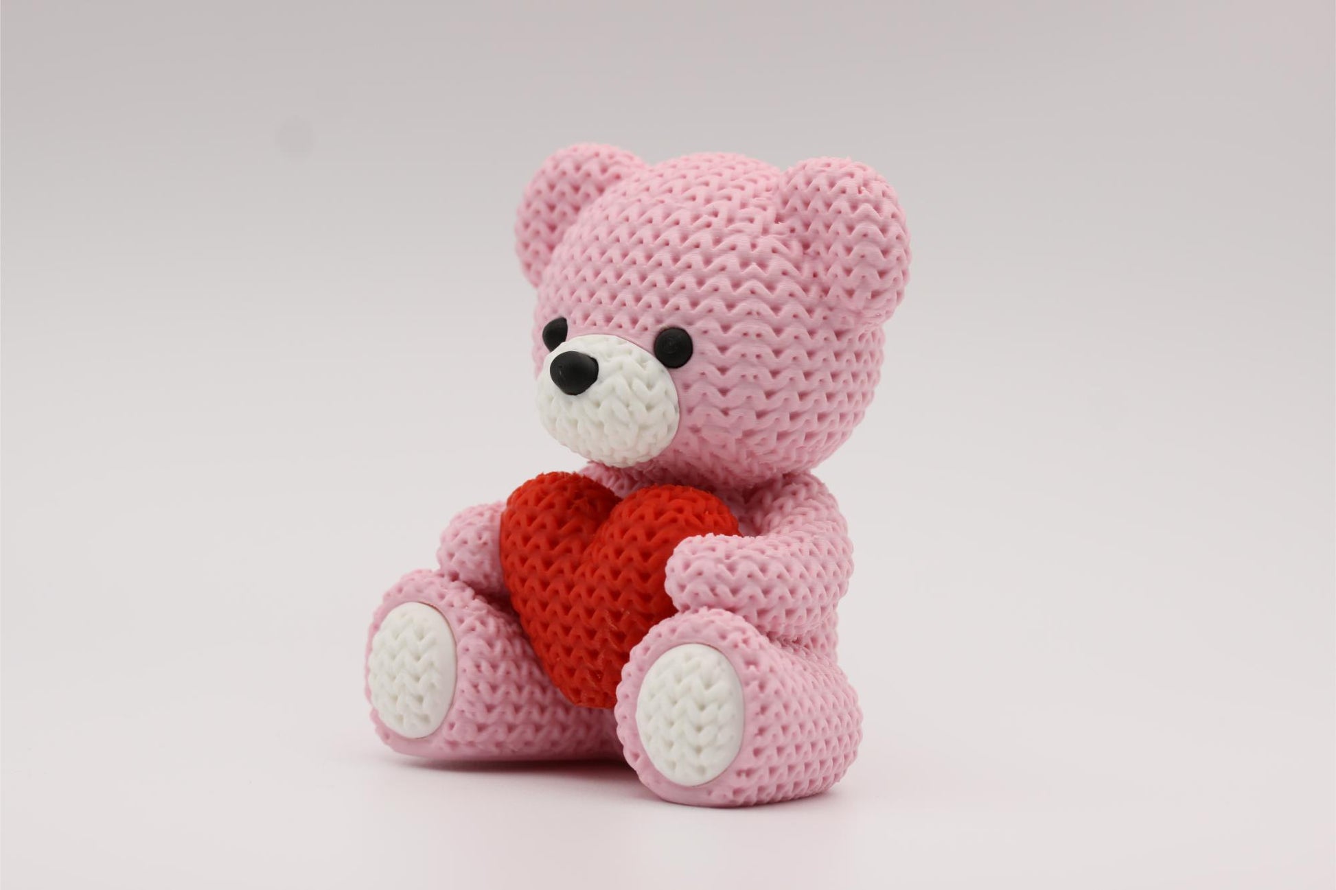3D-printet figur av en rose teddybjørn i strikket design som holder et hjerte